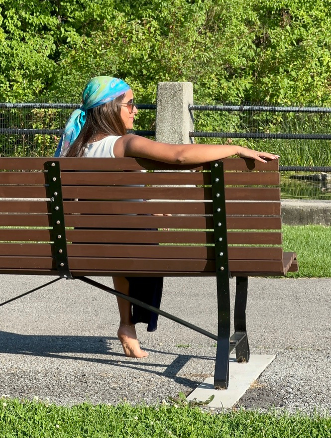 Luxury Silk Scarf Woman sitting on a park bench with greenery in the background