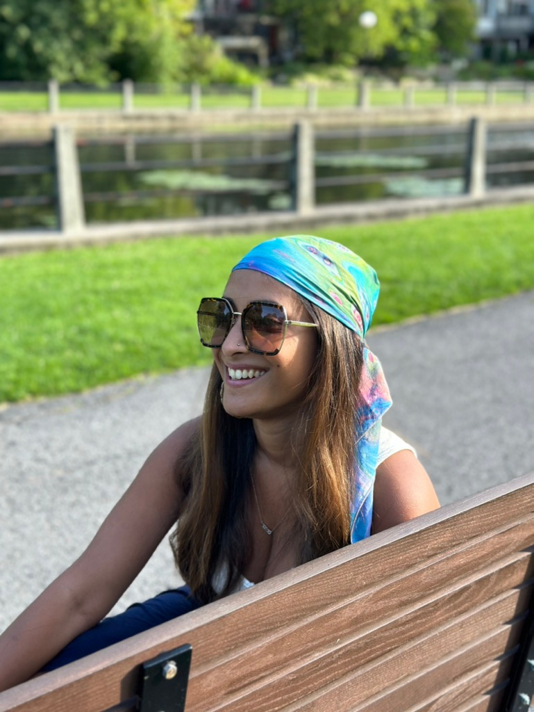 Woman wearing a colorful headscarf and sunglasses outdoors by a lake